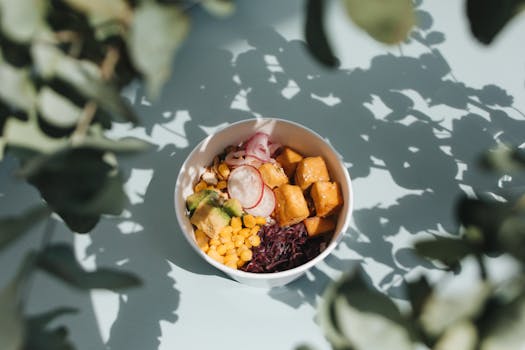 Top view of a vibrant poke bowl with tofu, avocado, and vegetables, surrounded by natural shadows.