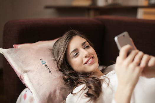 A woman smiling while using her phone, relaxing on a comfortable couch indoors.